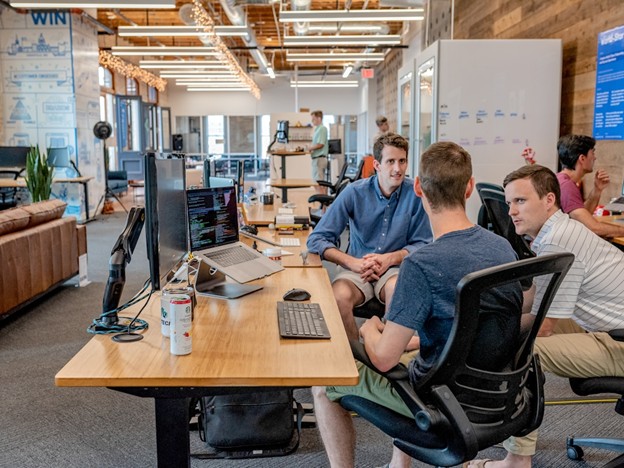 Three men discussing knowledge management software while seated at a table in an office setting.